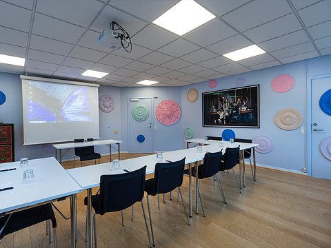 Mødelokale med borde, stole og farverige vægdekorationer