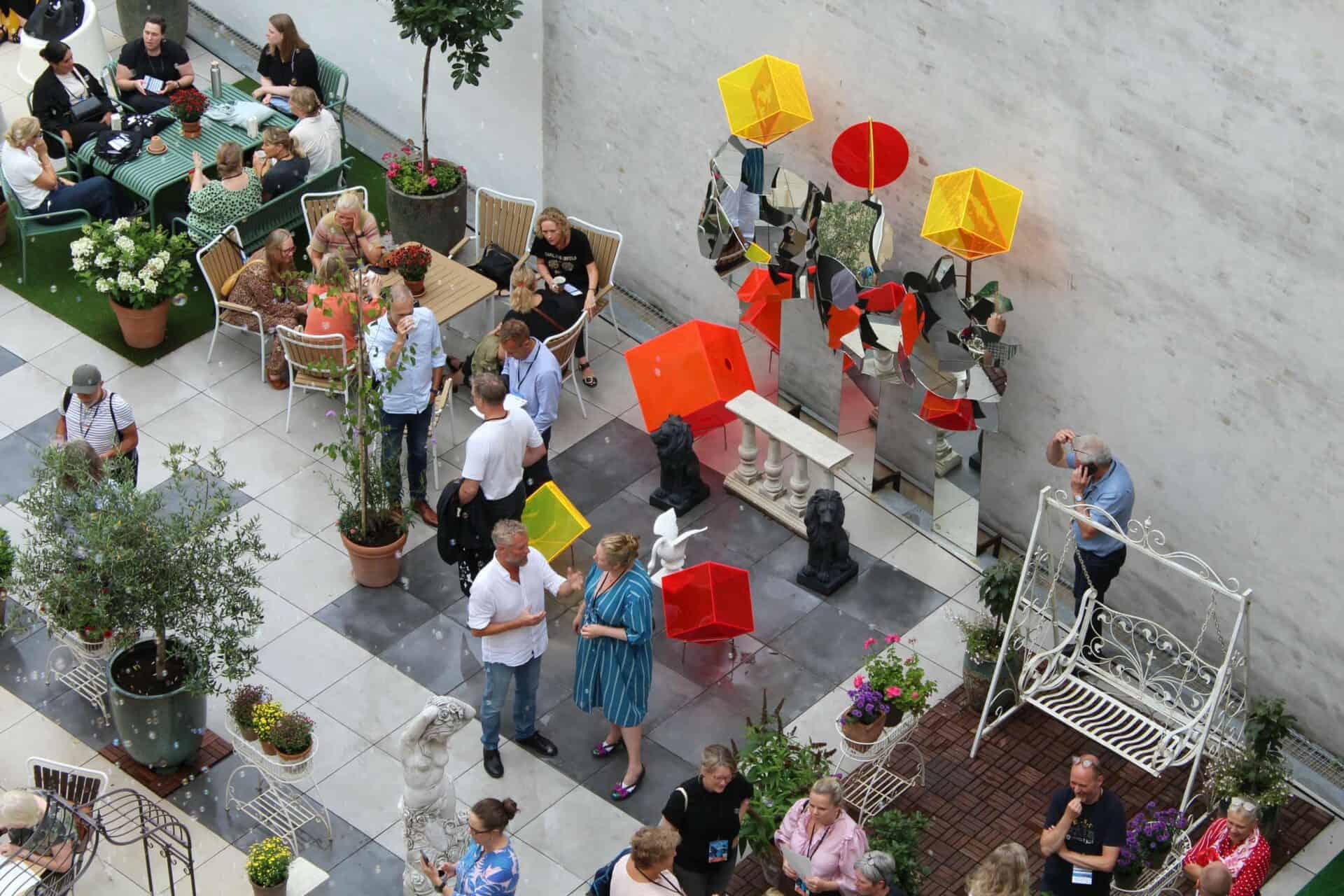 Folk samles i et udendørs mødeområde med kunstinstallationer