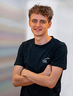 Ung mand med krøllet hår, iført sort t-shirt, smilende