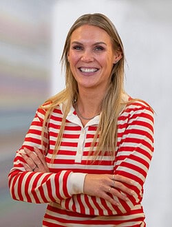 Kvinne med langt hår og stribet trøje står med armene over kors