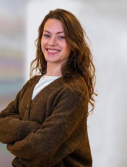 Smilende kvinde med brunt krøllet hår iført en brun cardigan